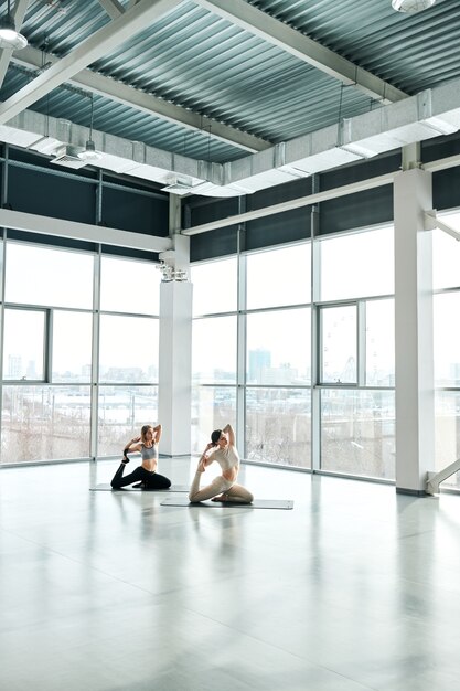 Jovens mulheres ativas em roupas esportivas praticando exercícios de ioga em esteiras durante o treino em uma grande academia ou centro de lazer