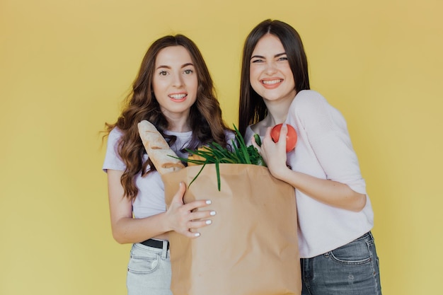 Jovens mulheres bonitas segurando o saco de papel da entrega sobre fundo amarelo estressado