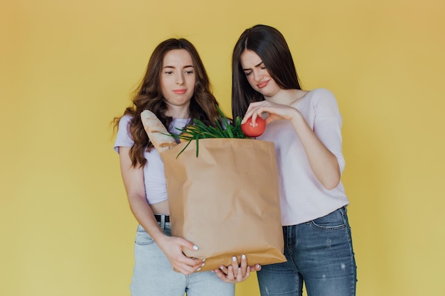 Jovens mulheres bonitas segurando o saco de papel da entrega sobre fundo amarelo estressado