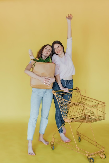 Jovens mulheres bonitas segurando o saco de papel da entrega sobre fundo amarelo