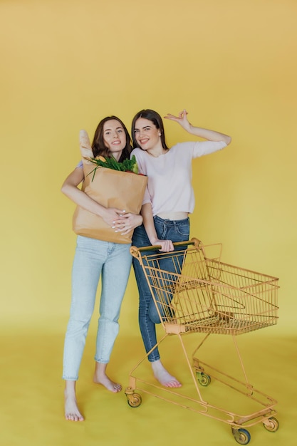 Jovens mulheres bonitas segurando o saco de papel da entrega sobre fundo amarelo