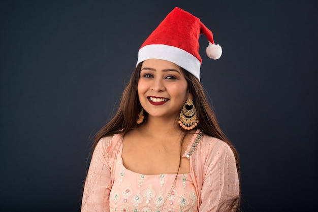 Jovens mulheres bonitas usando chapéu de Papai Noel comemorando o Natal posando e sorrindo em fundo cinza