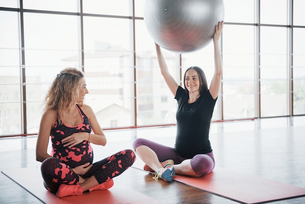 Jovens mulheres grávidas sentadas nas carruagens e segurando uma bala para exercícios.