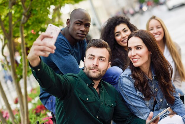 Jovens multi-étnicos que tomam o selfie juntos em um fundo urbano