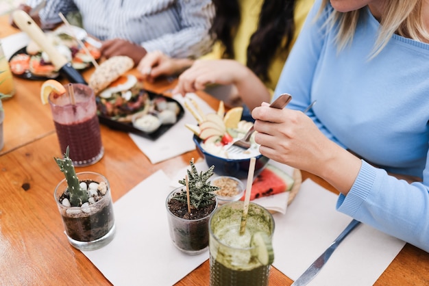 Jovens multirraciais comendo brunch e bebendo smoothies no bar restaurante - foco na mão direita da garota