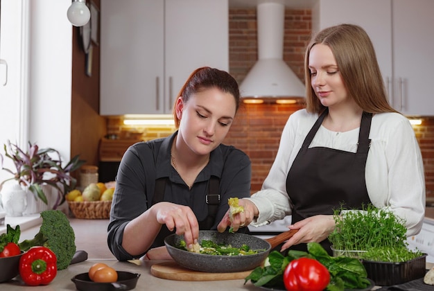 Jovens namoradas na cozinha cozinhando uma refeição vegetariana juntos