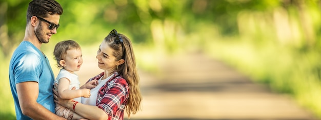 Jovens pais com filha, desfrutando de momentos juntos no parque - banner panorâmico.