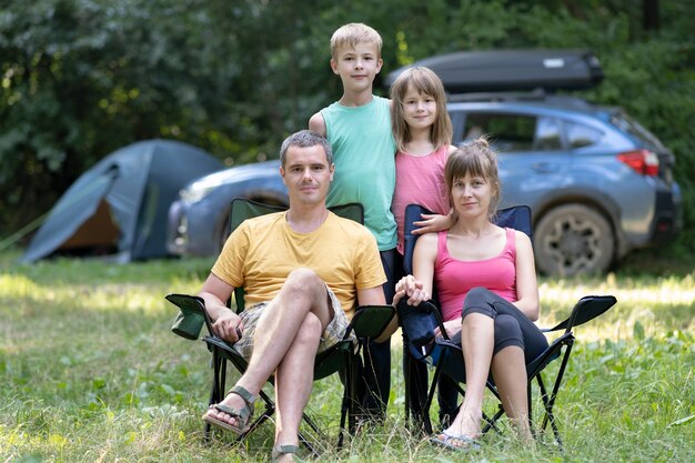 Jovens pais felizes e seus filhos descansando juntos em um acampamento no verão