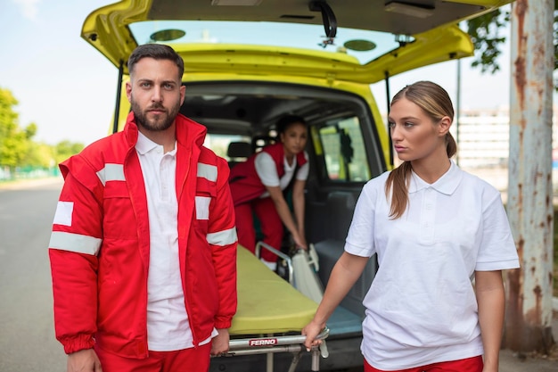 Foto jovens paramédicos movendo maca de ambulância do carro paramédicos de uniforme tirando maca do carro de ambulância