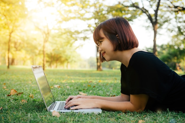 Jovens pernas da mulher asiática na grama verde com laptop aberto