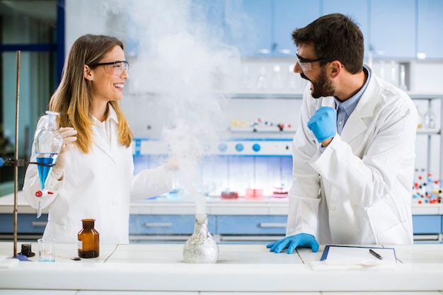 Jovens pesquisadores fazendo experimentos com fumaça na mesa de um laboratório químico