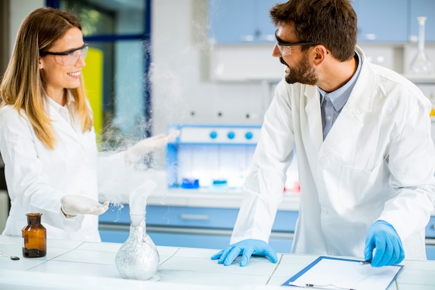 Jovens pesquisadores fazendo experimentos com fumaça sobre a mesa de um laboratório químico