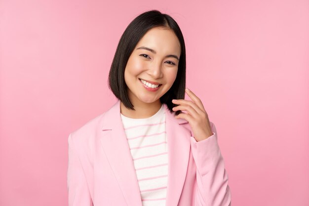 Jovens profissionais Sorrindo empresária asiática vendedora de terno parecendo confiante na câmera posando contra fundo rosa