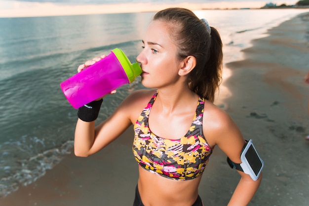 Jovens se encaixam garota bebendo água na praia após treino de manhã