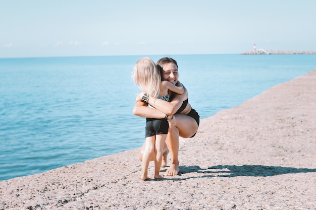 Jovens se encaixam mãe mãe com menina bonita exercitando juntos na praia
