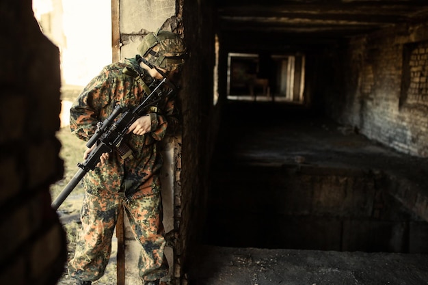 jovens soldados com armas, um soldado em equipamentos e com armas inspeciona uma casa em ruínas fora da cidade.