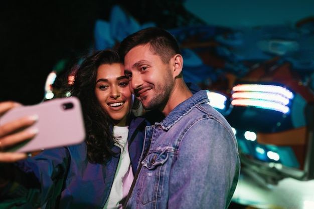 Jovens sorridentes tirando selfie à noite em um parque de diversões