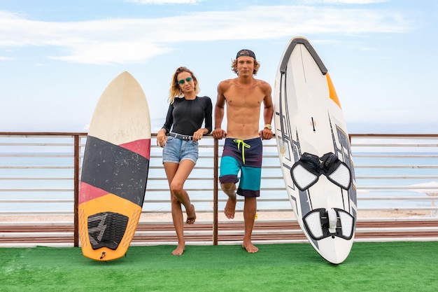 Jovens surfistas ativos sorridentes relaxando na praia depois do esporte com Surfboard Healthy Lifestyle Extreme Water Sports