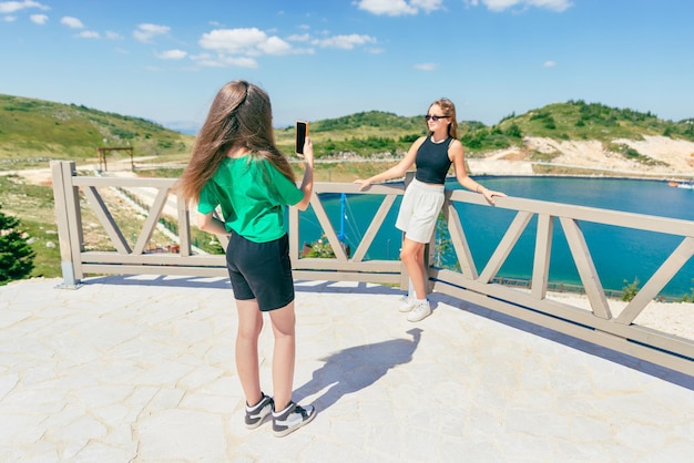 Jovens tirando fotos com telefone umas das outras Turistas adolescentes na montanha à beira do lago