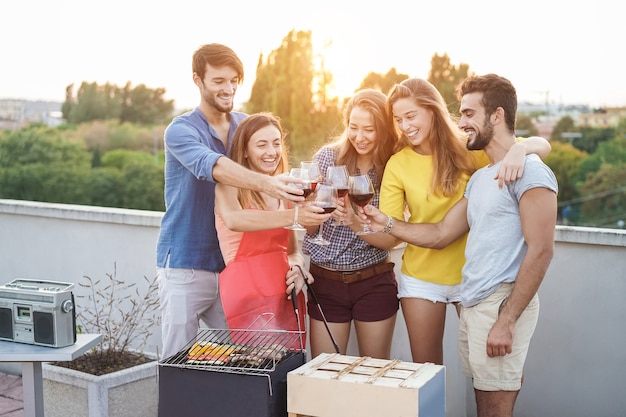 Jovens torcendo com vinho na festa de churrasco ao ar livre no terraço - foco em taças de vinho