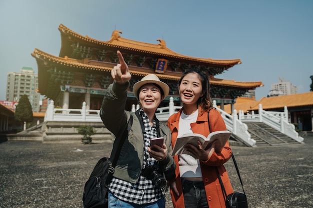 Jovens turistas asiáticos segurando o celular do livro guia no destino de viagem em bangkok, tailândia. viagem de verão de viajantes de mulher japonesa na china visitam o templo de pequim. menina feliz apontar o dedo