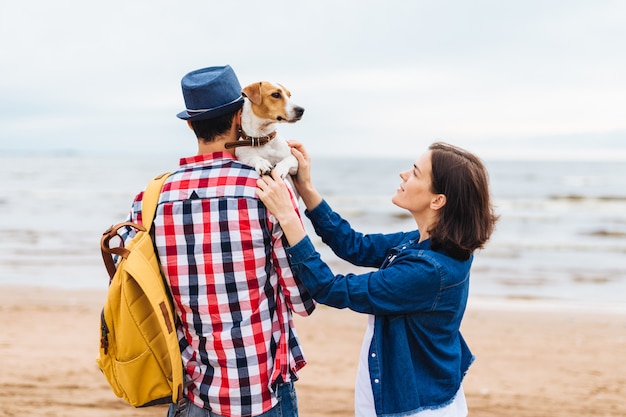 Jovens turistas masculinos e femininos caminharam perto do mar, carregam seu animal de estimação favorito