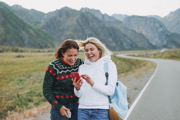 Jovens viajantes felizes usando celular na estrada contra a bela paisagem montanhosa