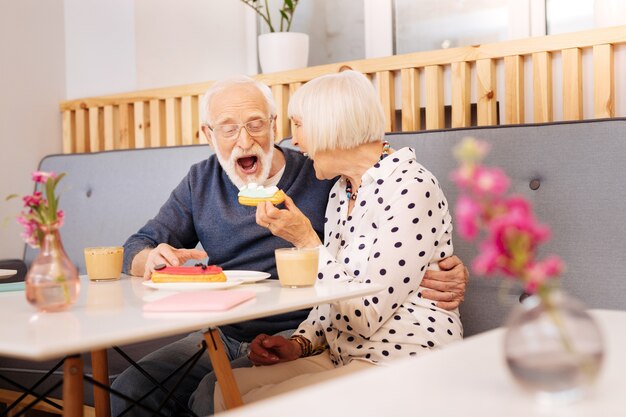 Jovial ältere Frau hält Eclair und älterer Mann beißt es