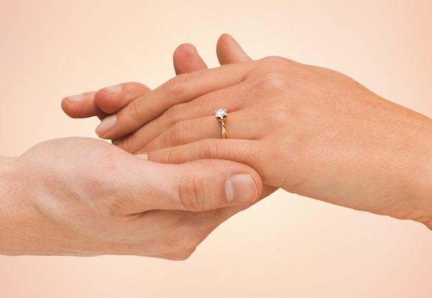 joyería, pareja, amor y concepto de boda - cierre de manos de hombre y mujer con anillo de compromiso sobre fondo beige