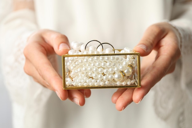 Joyero con perlas y anillos de boda en manos femeninas sobre fondo claro