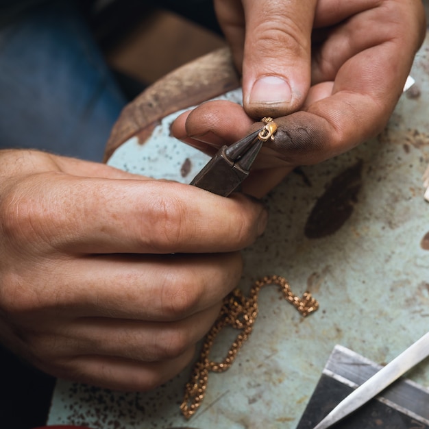 Un joyero repara un candado en una cadena de oro, un primer plano de un flujo de trabajo