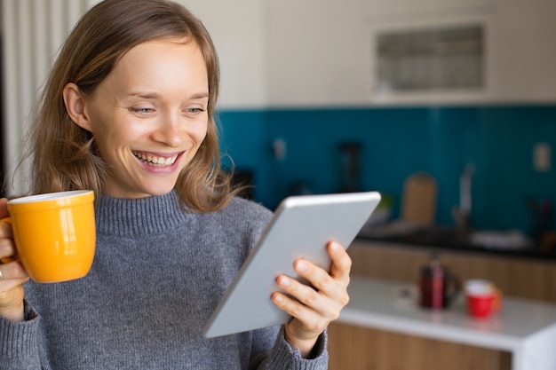 Joyful Lady Drinking Tea y Using Tablet at Home