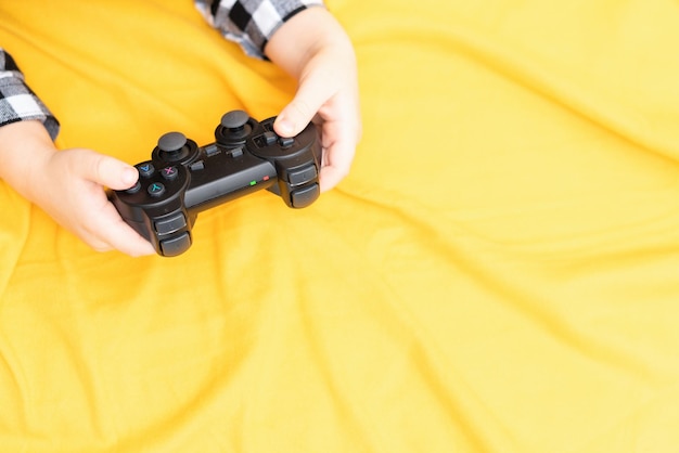 Joystick preto para jogar o videogame em mãos de criança no fundo de tecido amarelo Jogando videogame no conceito de casa Passar tempo juntos Estilo plano leigo com espaço de cópia