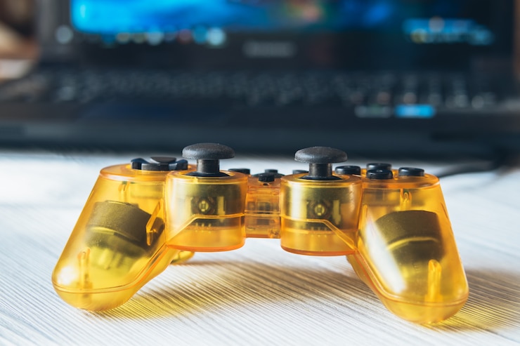 Joystick transparente amarelo e um laptop com um videogame em uma mesa
