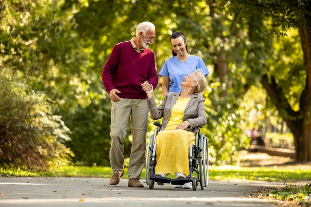 Foto jubilación feliz las personas mayores en silla de ruedas y la enfermera asistente disfrutan caminando en el parque