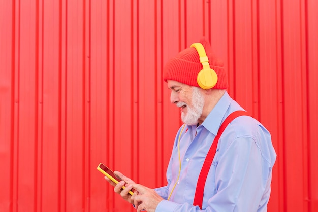 Un jubilado moderno escuchando música con auriculares mientras usa su teléfono móvil