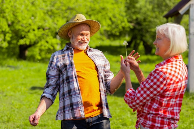 Jubilados alegres. Alegre pareja de jubilados que se sienten felices después de soplar el diente de león