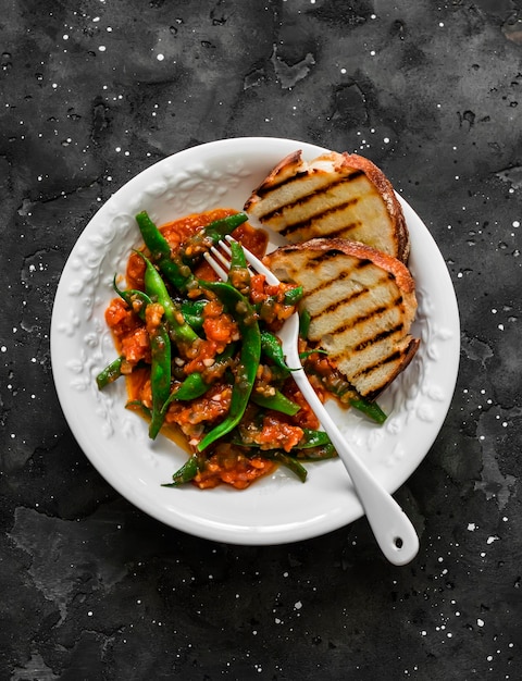 Judías verdes en salsa de tomate y pan a la parrilla delicioso refrigerio vegetariano en una vista superior de fondo oscuro