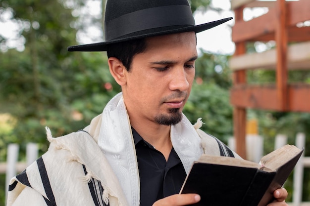 Un judío latino con tallit y sombrero judío leyendo las escrituras en la tranquilidad de su patio