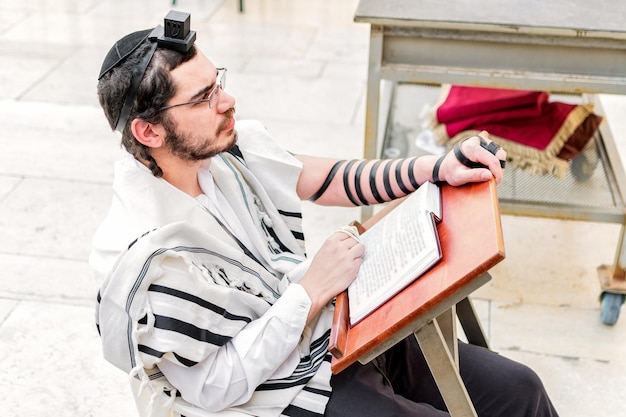 Judío ortodoxo hombre vestido con phylacteries tefilin y mantón tallit sentado orando en el Muro de las Lamentaciones de Jerusalén