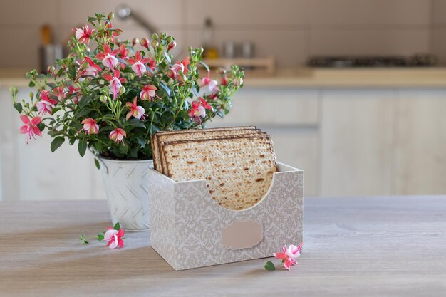 Jüdischer Feiertag Pessach-Hintergrund Matzah in einer speziellen Box mit einer Inschrift matzo fuchsia Blume auf dem Küchentisch