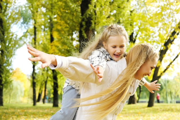 Juega a volar o madre con niña en la espalda en el parque de otoño