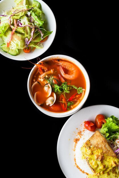 Juego de almuerzo hecho de sopa tom yum, ensalada, pescado basa a la parrilla, arroz, sobre fondo negro