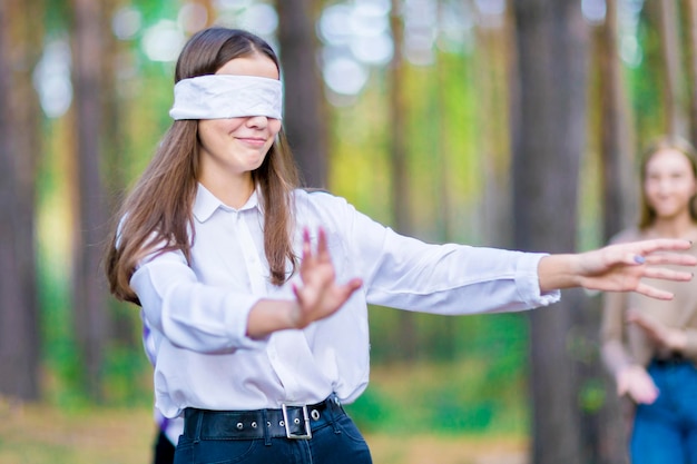 El juego de la bufonada del ciego Niña sonriente con los ojos vendados Adolescentes en el bosque de verano Primer plano