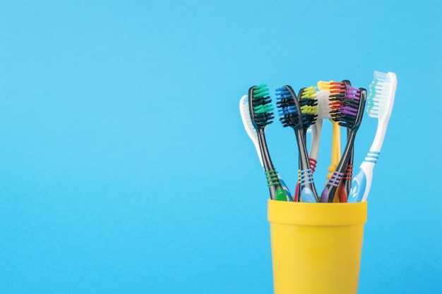 Un juego de cepillos de dientes en un vaso de plástico amarillo sobre un fondo azul.