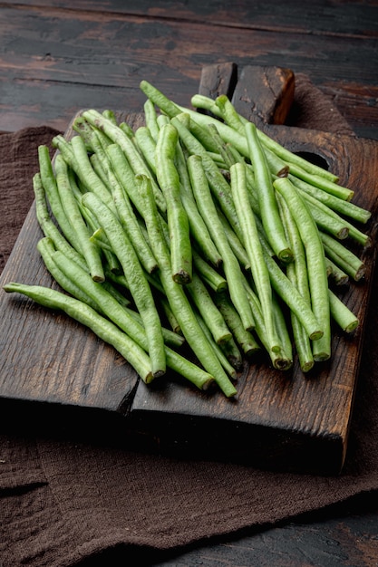 Juego de cocina de judías verdes, sobre tabla de cortar de madera, sobre fondo antiguo de mesa de madera oscura.