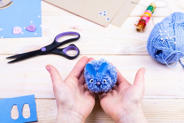 Un juego de costura sobre una mesa de madera. Hilos, tijeras, papel para hacer un conejo con pompones.