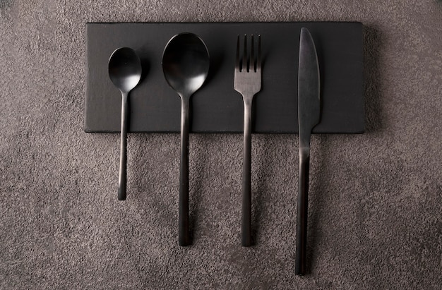 Juego de cubiertos negro - tenedor, cuchara, cuchillo, sobre madera oscura. Bodegón minimalista, vajilla elegante.