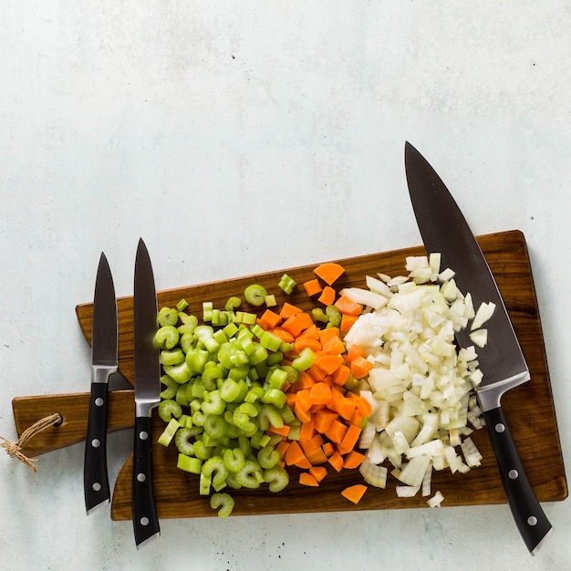 Foto juego de cuchillos sobre una tabla de cortar de madera y verduras picadas