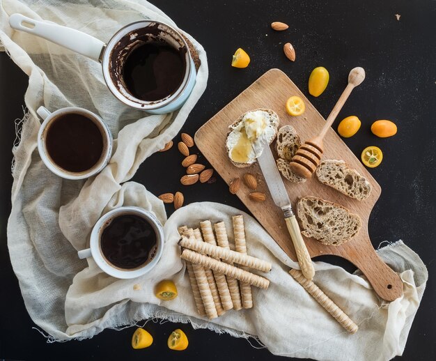 Juego de desayuno olla o cezve de taza de café en una toalla de cocina kumquats peras rebanadas de baguette de pomelo con crema de mantequilla y tablero de madera rústica de miel sobre fondo negro